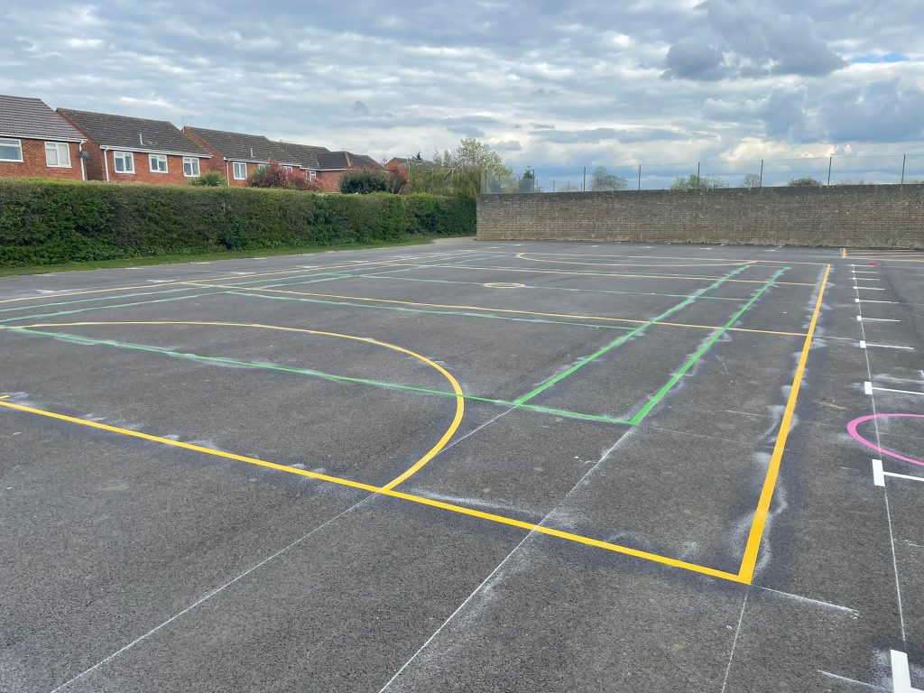 Newly laid yellow, green and white sports court markings on a tarmac games area, with chalk setting-out marks still visible