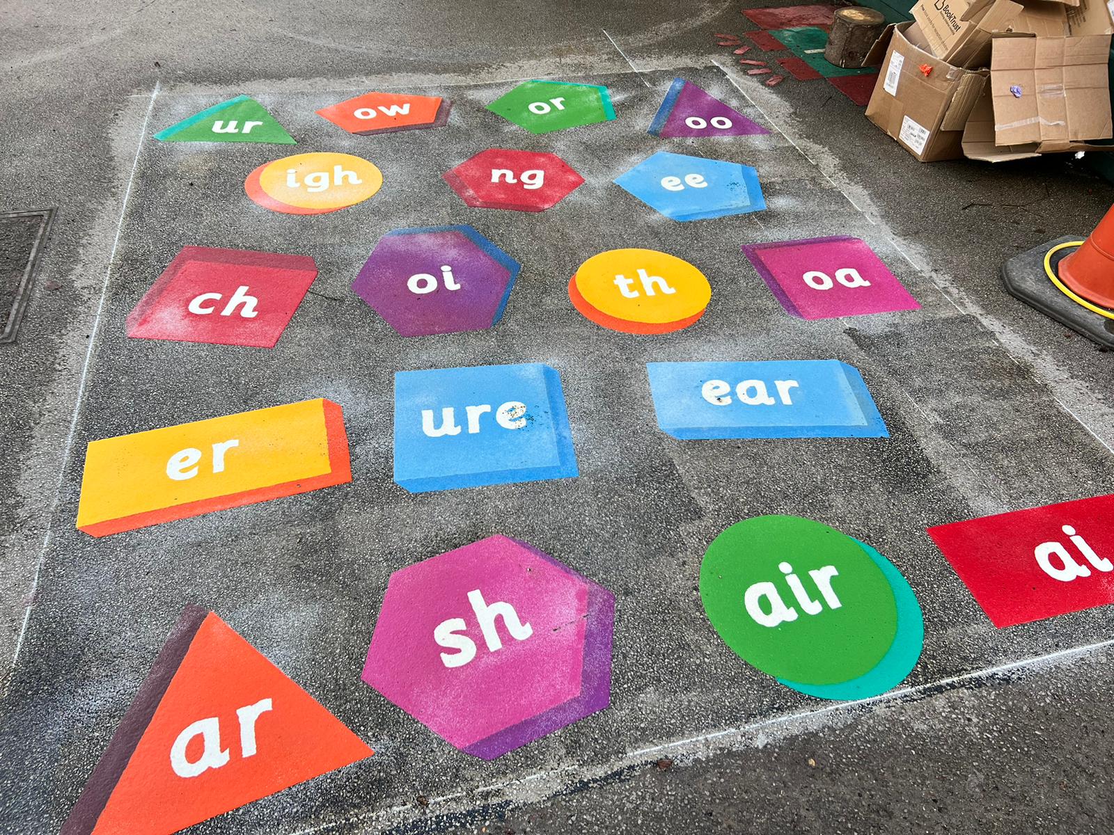 Freshly laid phonics markings with 3D-effect shapes for sounds such as sh, air, ure and igh inside chalked setting-out lines