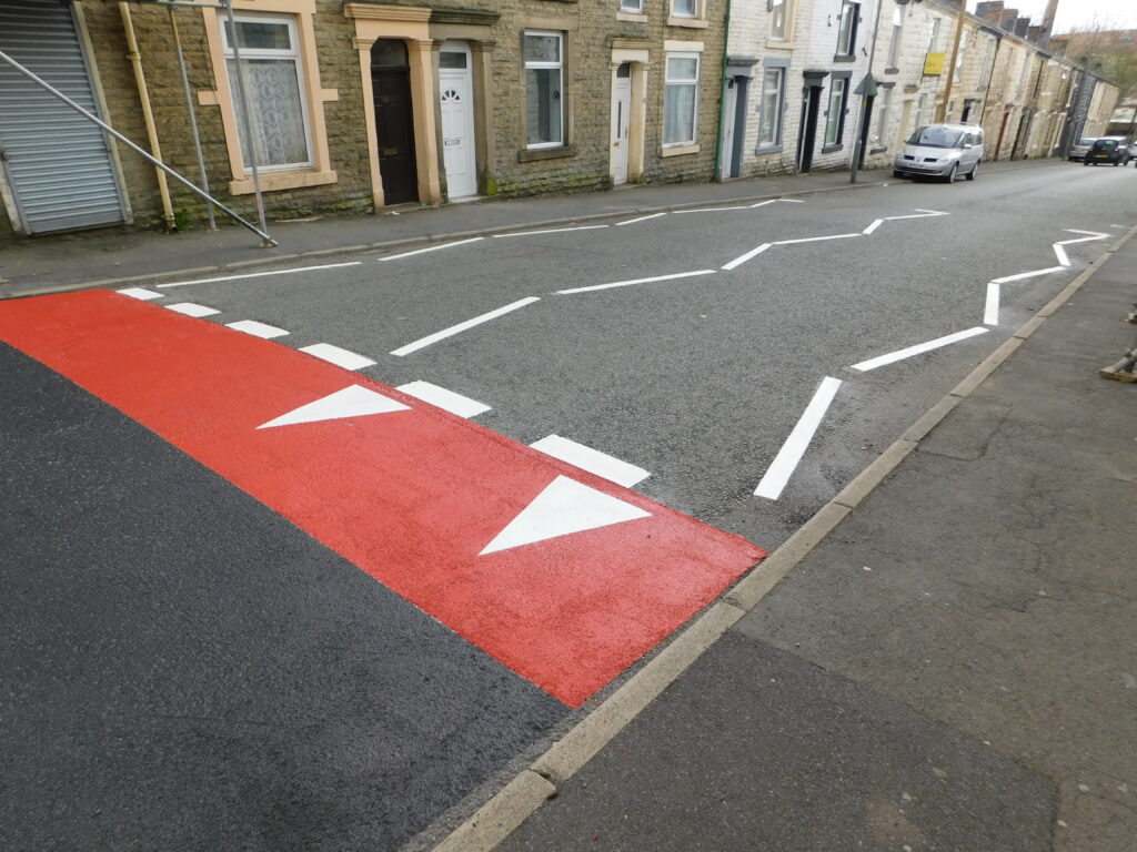 Thermoplastic road markings on a terraced street, with a red road hump, white triangles and white zigzag lines
