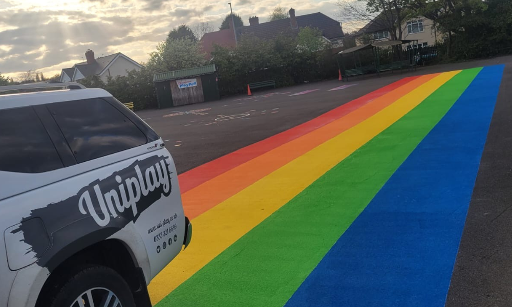 Uniplay vehicle parked beside a wide rainbow stripe of thermoplastic markings running across a school playground