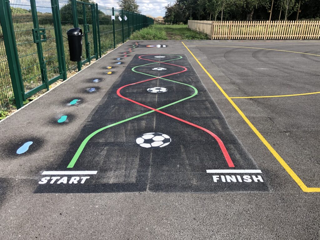 Football skills track marking with red and green weaving lines between start and finish, beside a footprint trail and fencing