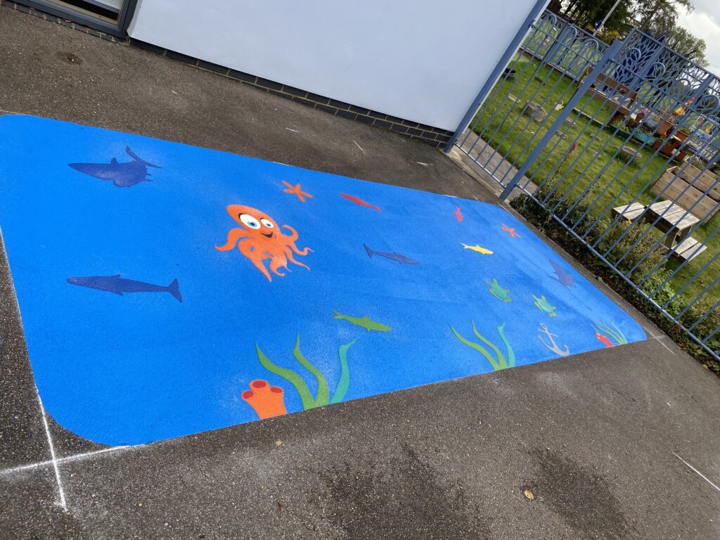 Blue under the sea panel with an orange octopus, sharks, fish and seaweed filling a narrow strip of playground by railings