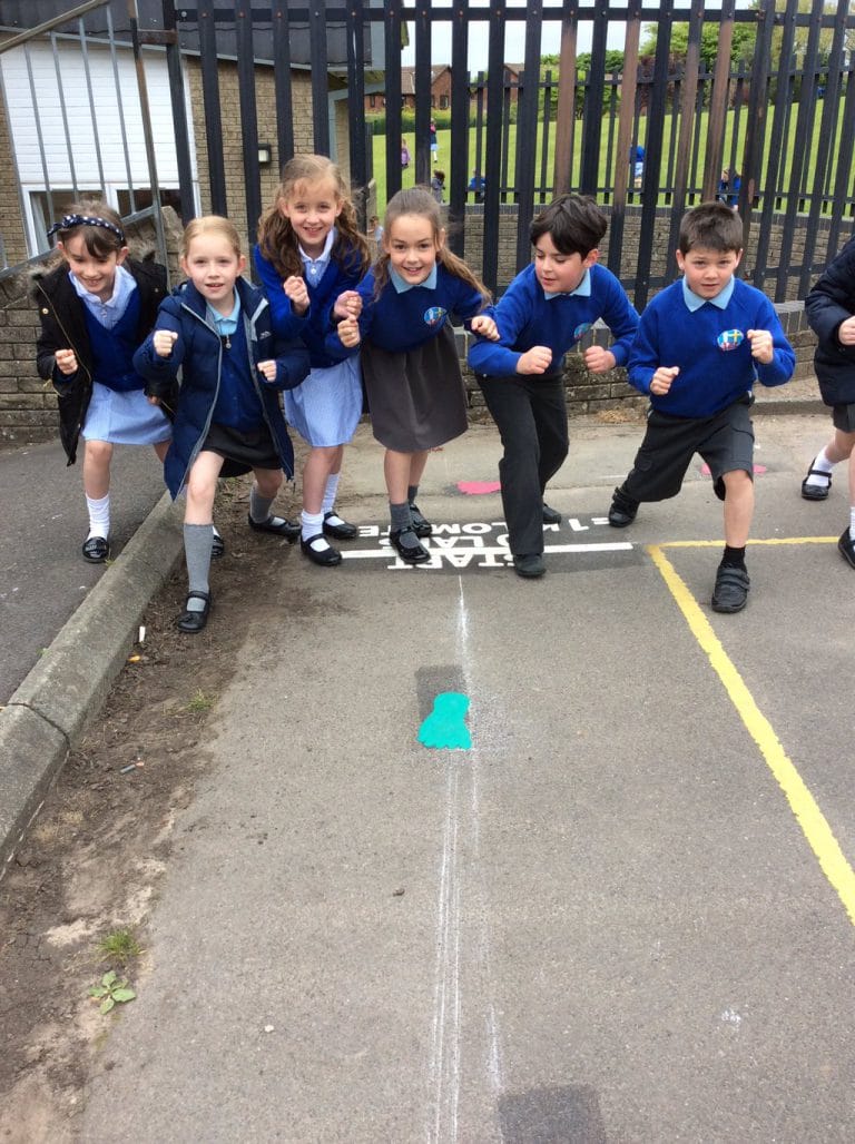 St Barnabas pupils in blue uniforms crouched ready to run at a 1 kilometre start line marking beside a turquoise footprint