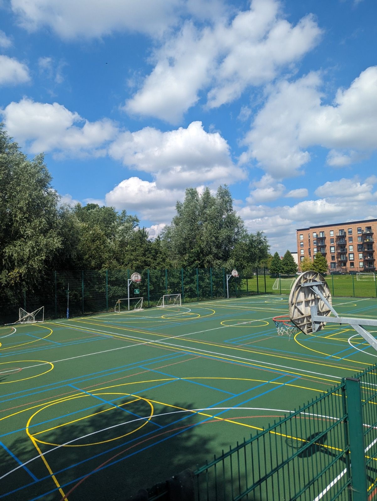 Green-coated multi-use games area with yellow, blue, white and red sports court markings, basketball hoops and goals