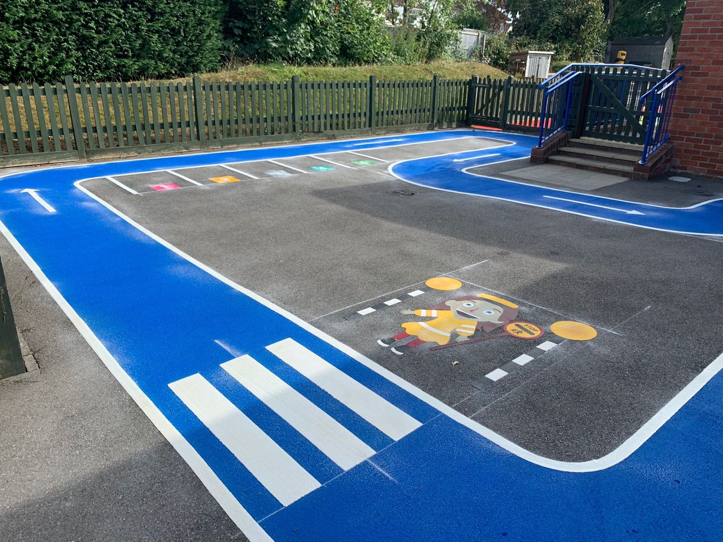Blue road-safety track marking with arrows, a zebra crossing, a lollipop lady figure and numbered bays in a school playground