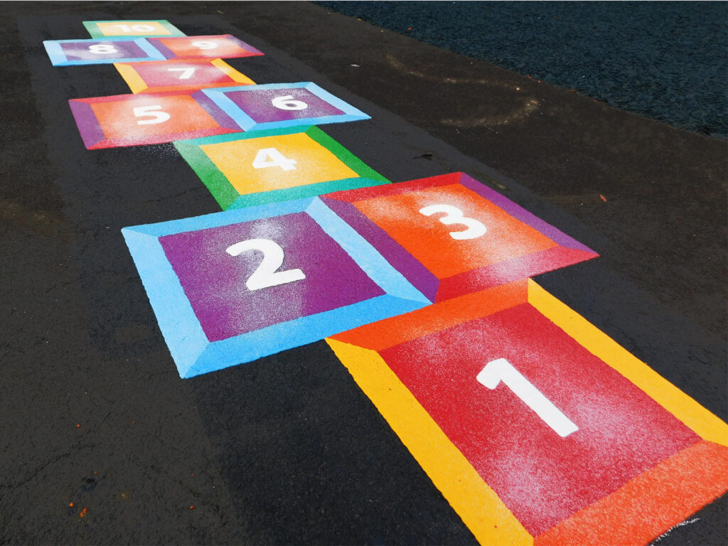 Thermoplastic hopscotch numbered 1 to 10 with bevelled 3D-effect squares in red, purple, orange and yellow on dark tarmac