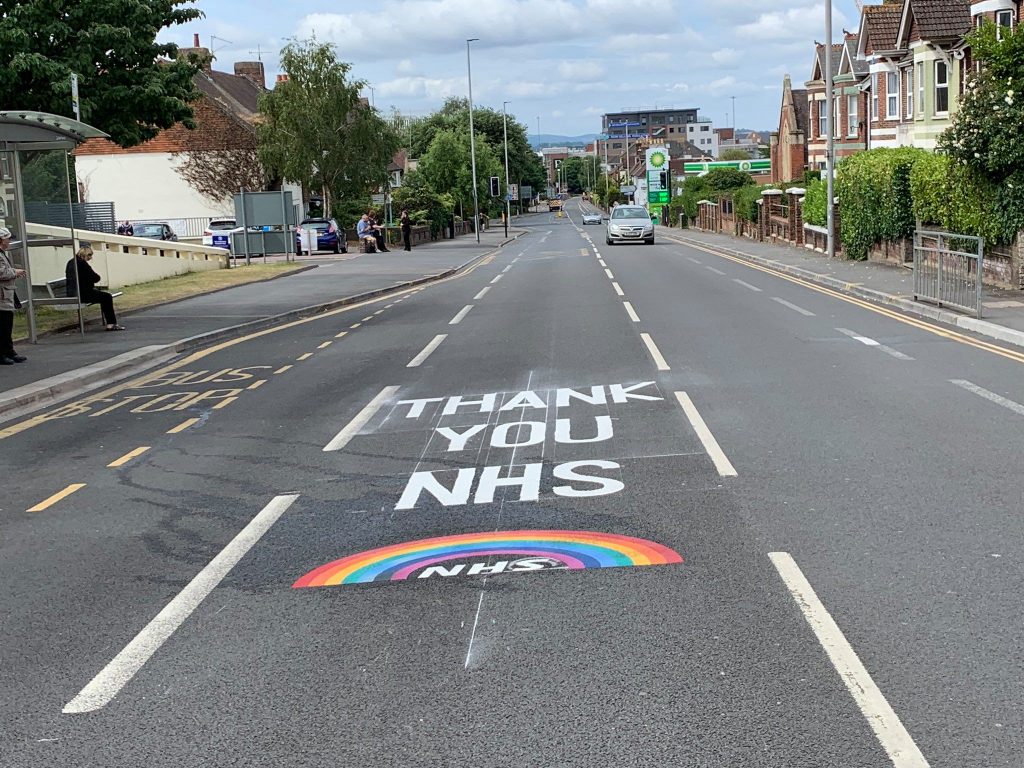 THANK YOU NHS road marking and rainbow NHS logo in preformed thermoplastic on a residential street beside a bus stop