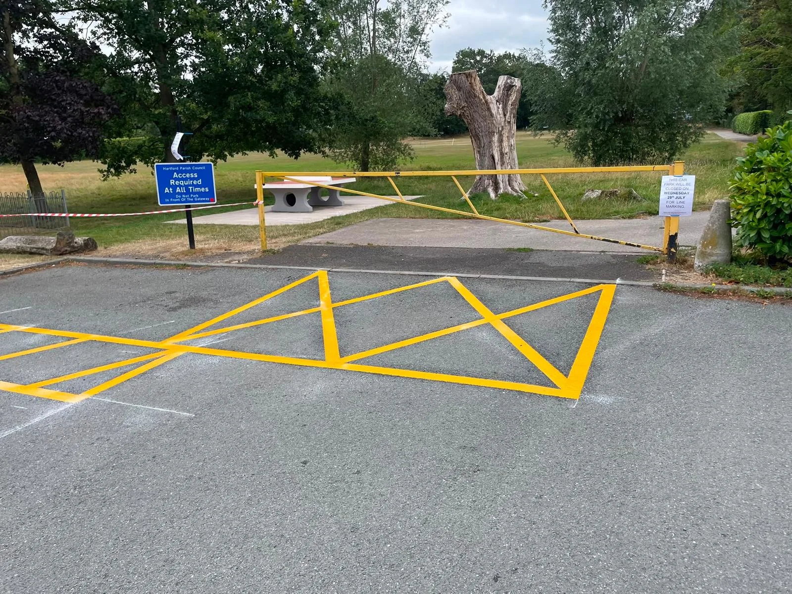 Yellow hatched no-parking zone in front of a park access barrier, beside a Hartford Parish Council access sign