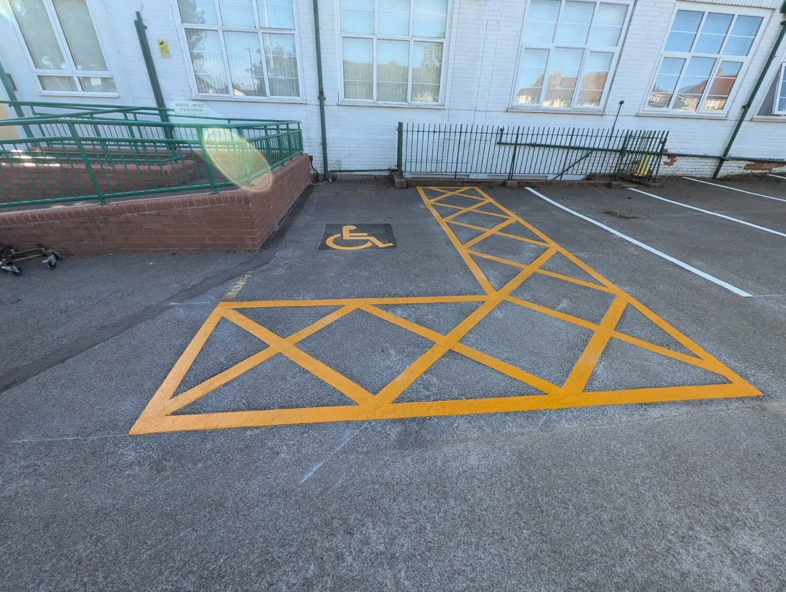 Yellow hatched no-parking marking and a wheelchair symbol bay outside a school office, with white parking bays alongside
