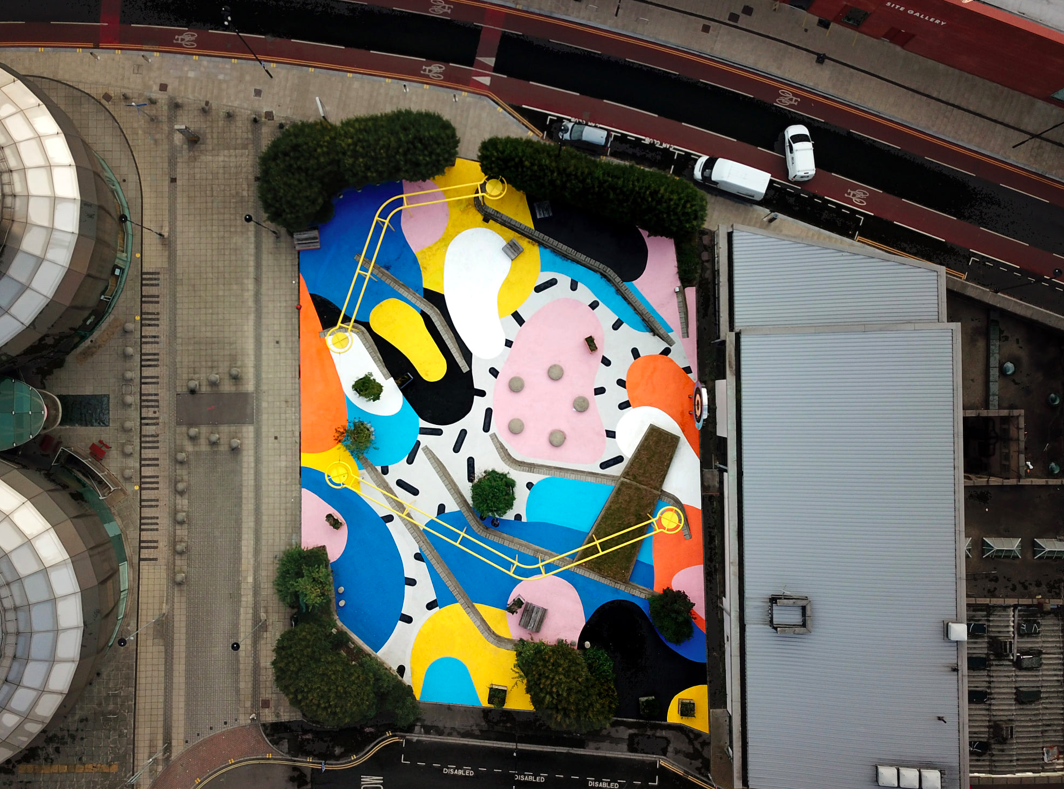 Aerial view of BOUNCE! by Florence Blanchard, a public square covered in pink, blue, yellow and orange abstract shapes