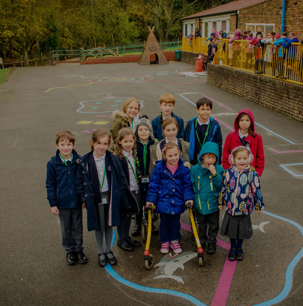 Halton Combined School pupils stand on a blue outlined shark marking, with a wooden tepee and children at railings behind