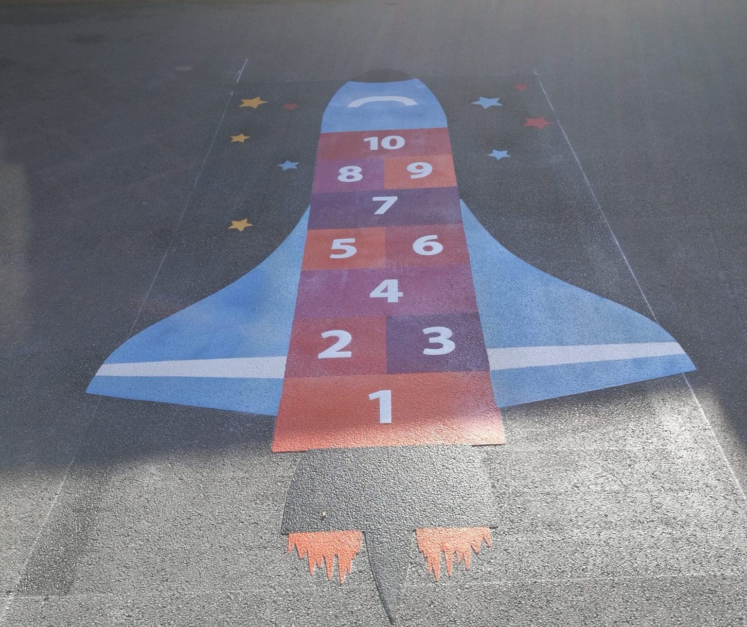 Thermoplastic space shuttle hopscotch numbered 1 to 10 in red and purple squares, with pale blue wings, orange flames and stars