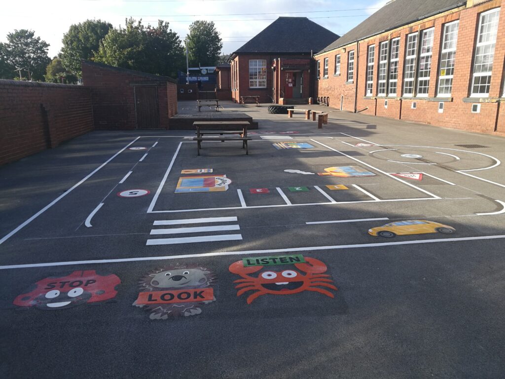 Road safety markings at Stanley St Peter's Primary School with a zebra crossing, roundabout and Stop, Look, Listen characters