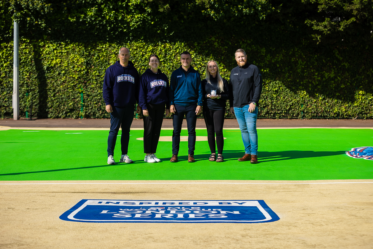 Five people, two in Rockets hoodies, pose on the green baseball field behind the MLB World Tour London Series badge