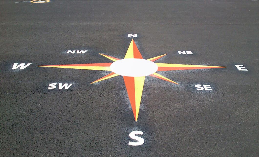 Compass rose marking with orange and yellow points and white N, E, S and W letters on the St Crispin's Infant School playground