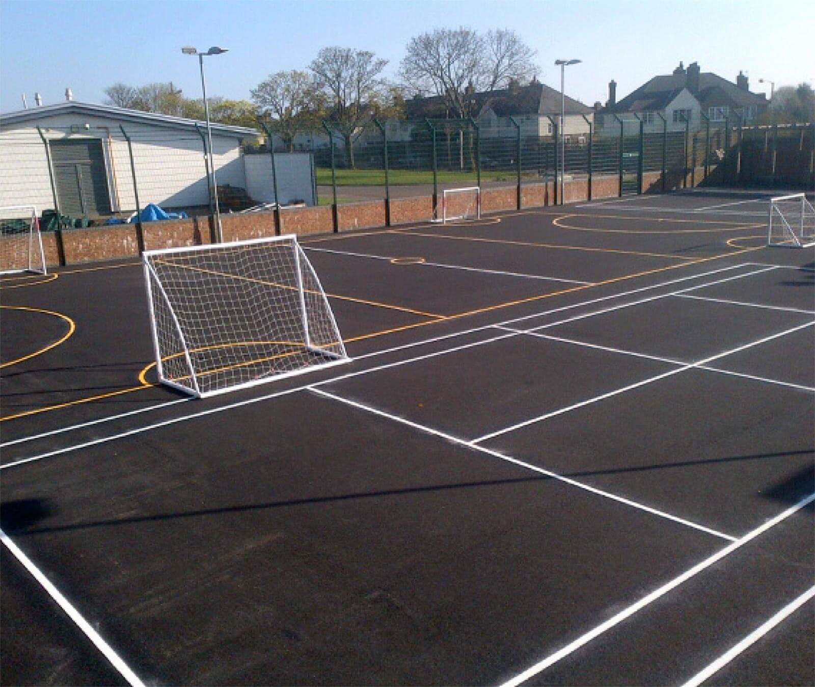 Fenced MUGA at St Vincents RC Primary School with white and yellow sports court markings and small football goals
