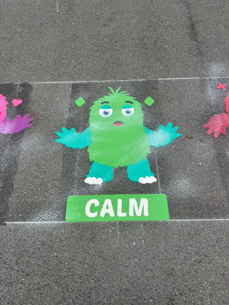 Colour Creatures emotion monster, a green furry figure above a CALM label on grey tarmac