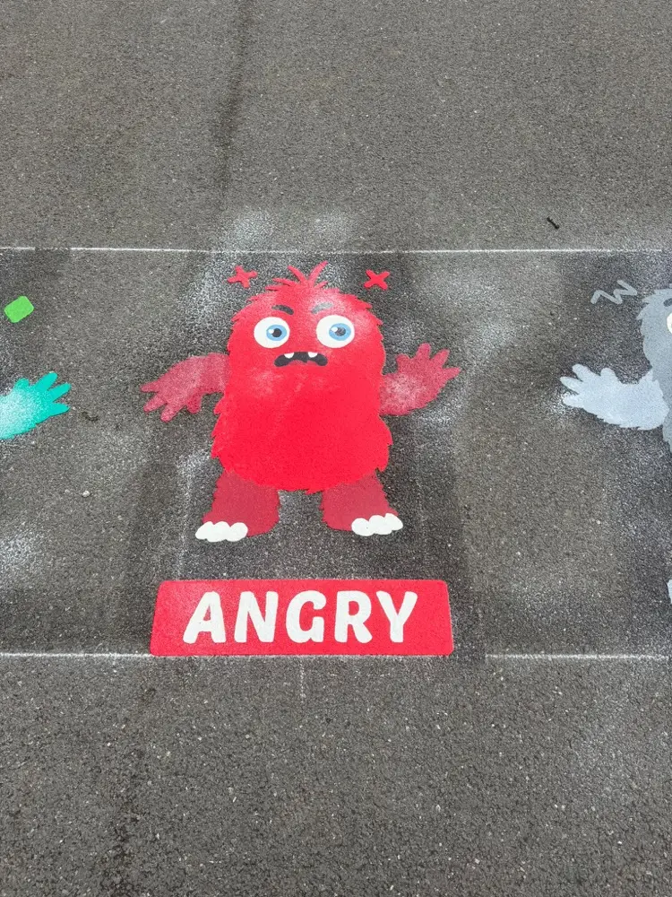 Colour Creatures emotion monster, a red furry figure above an ANGRY label on grey tarmac