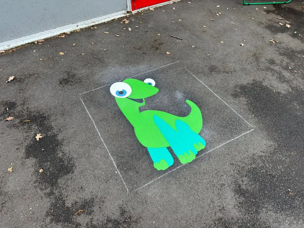 Standing green dinosaur marking with turquoise legs and blue eyes on a wet playground near a building wall