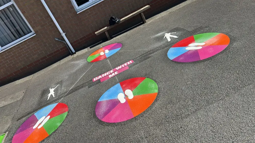 Dance With Me dancing discs beside a brick wall and bench, white footprints on each coloured circle