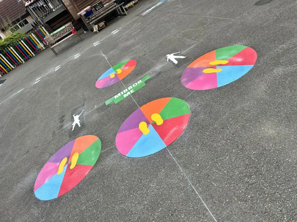 Dance With Me footprint discs in rainbow segments across open tarmac with storage trolleys behind