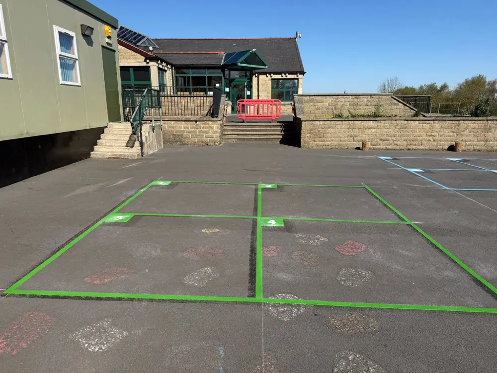 Green numbered Four Square Game marking on a sunlit tarmac playground in front of a stone school building