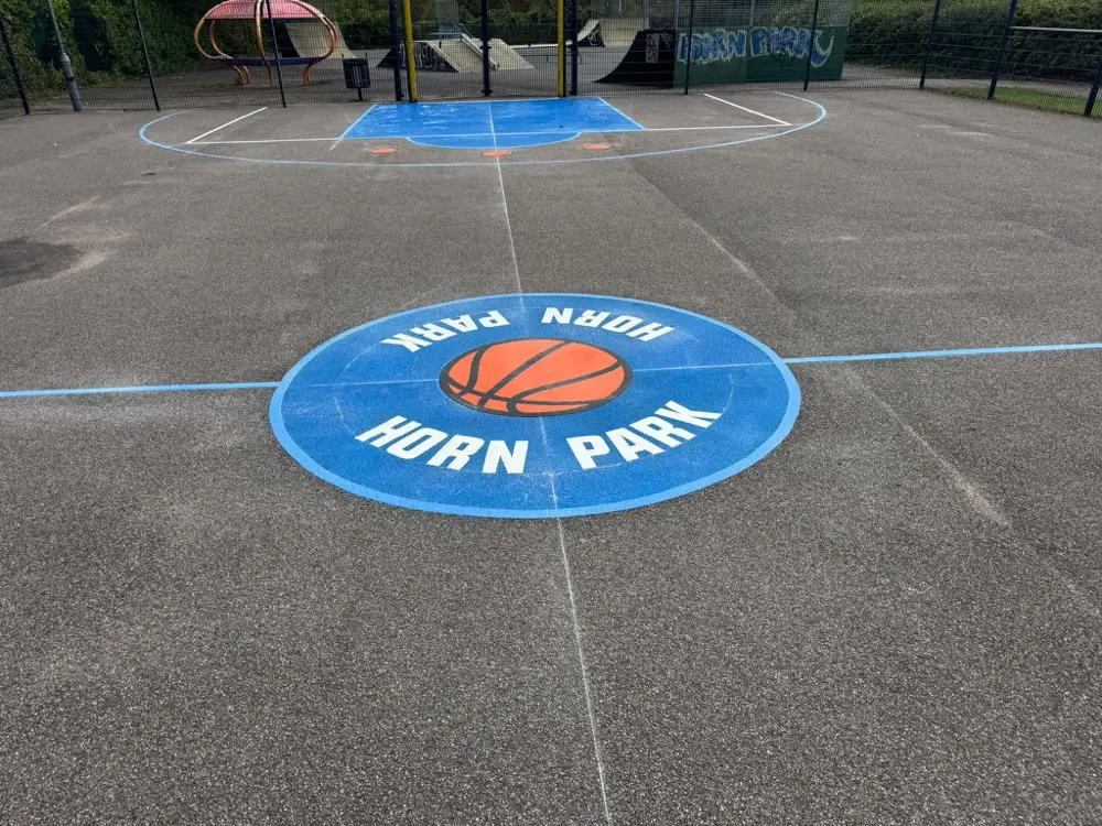 Blue basketball court with a school crest in the centre circle, key markings beside a skate ramp area