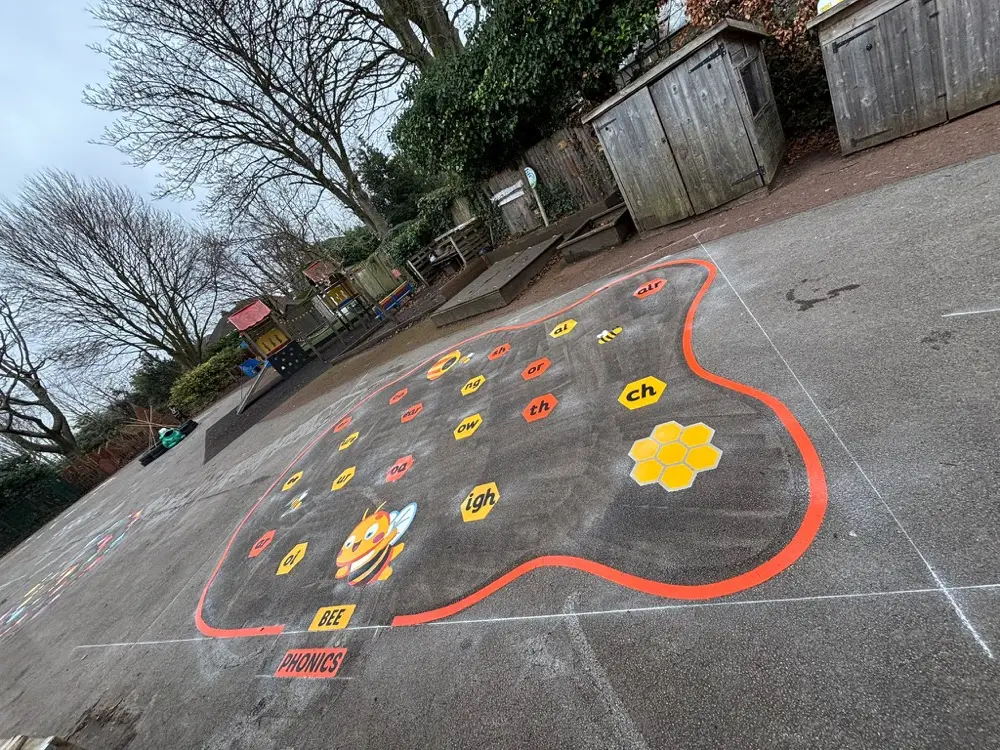 Bee Phonics mat shot at an angle on wet tarmac, honeycomb cluster and bare winter trees beyond