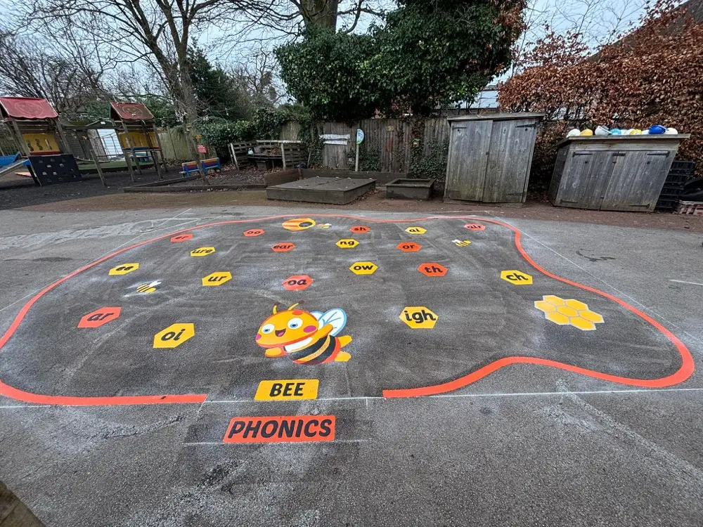 Bee Phonics sound mat ringed in orange with phoneme tiles and a cartoon bee, playground behind