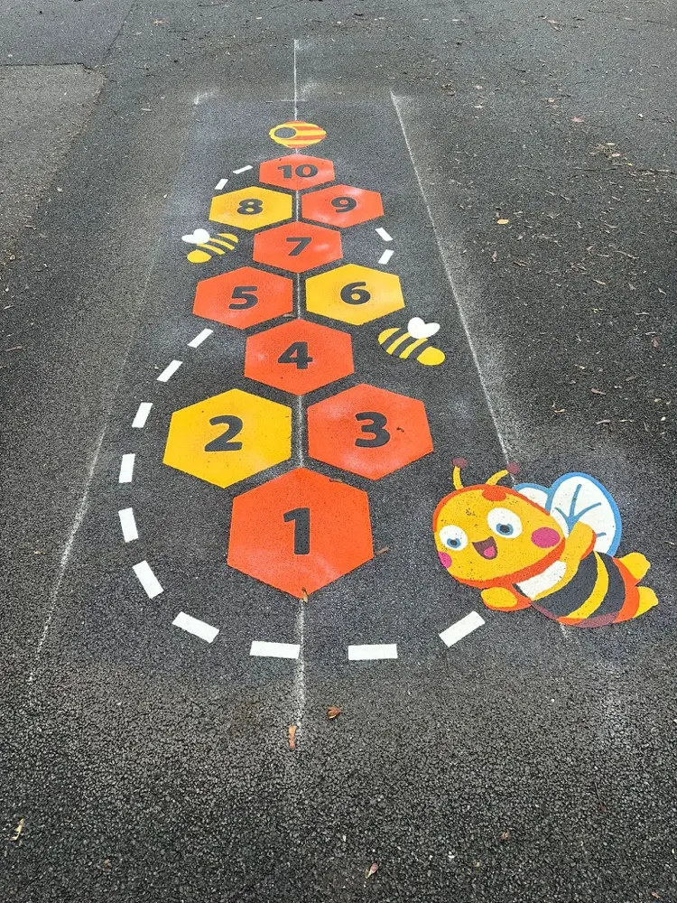 Bee Hopscotch with orange and yellow honeycomb hexagons and a cartoon bee on grey tarmac