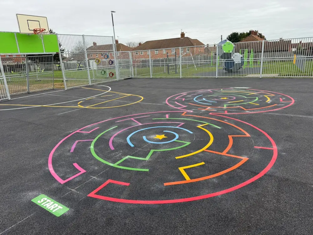 Rainbow double circular maze marking with a green START box on a fenced playground beside a basketball hoop