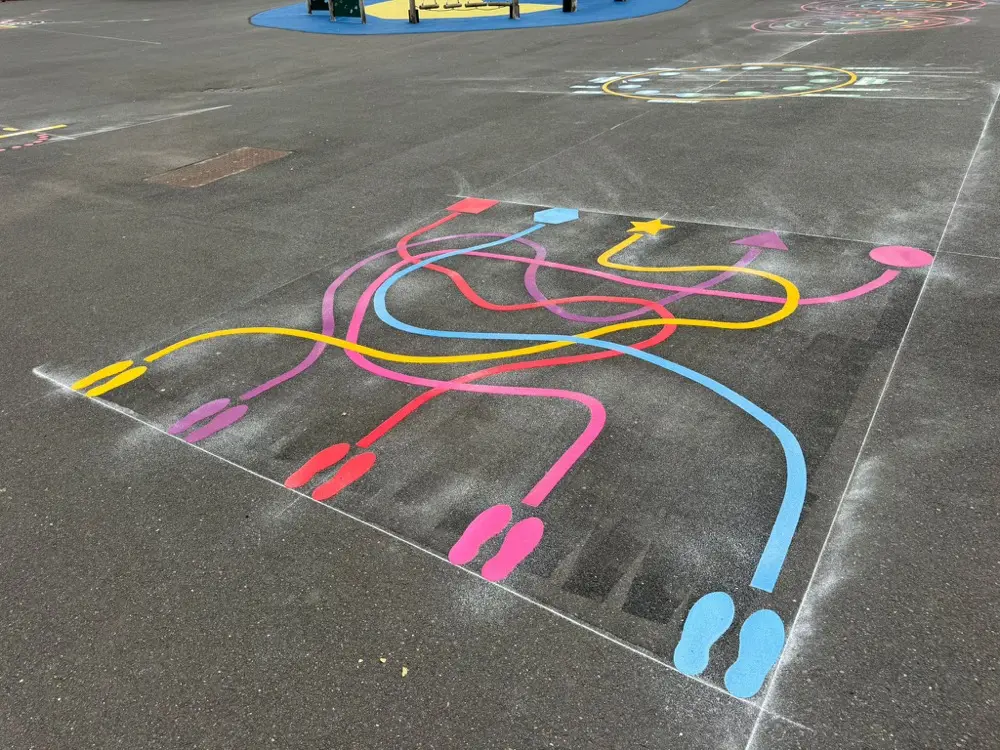 Colourful Line Maze with footprint and arrow endpoints viewed across a wide tarmac playground with play equipment behind