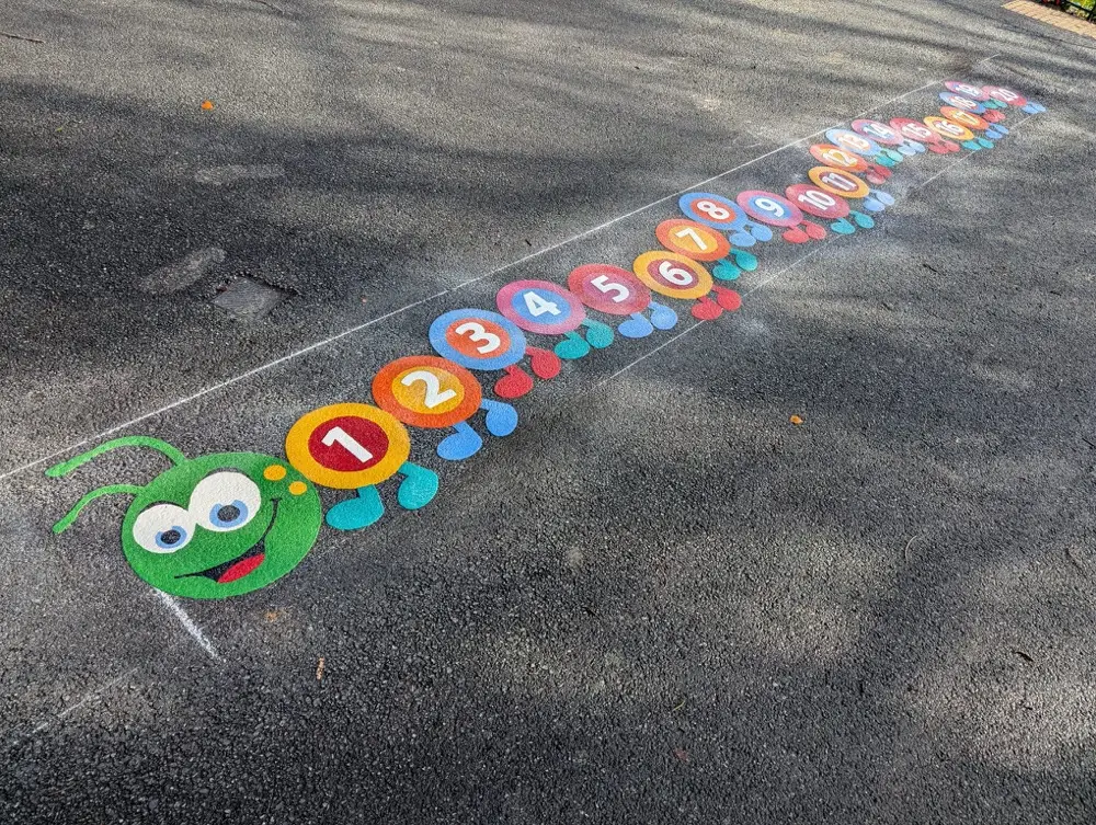 1 to 20 Caterpillar stretching into the distance across dappled playground tarmac, smiling green head close up
