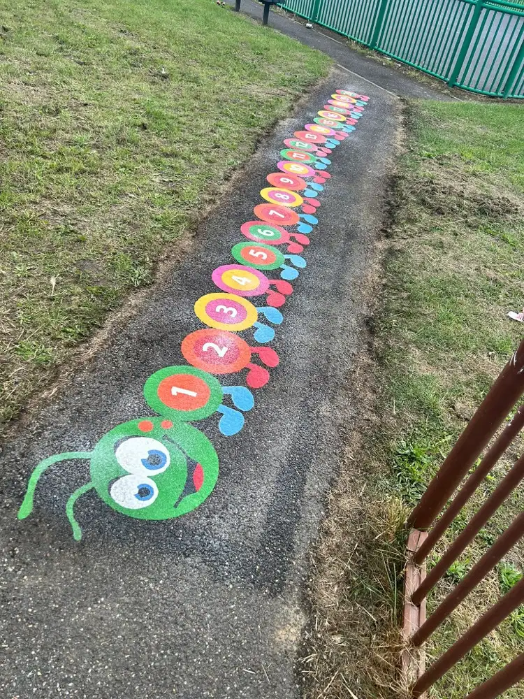 1 to 20 Caterpillar winding up a worn tarmac path towards a green fence, green-faced head in front