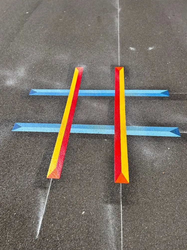 Red, yellow and blue Noughts and Crosses grid with a 3D effect on grey tarmac