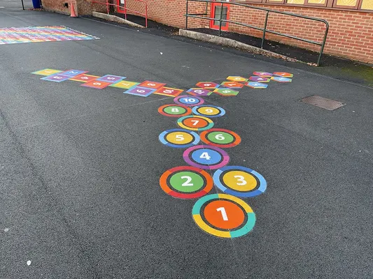 Ringed thermoplastic hopscotch numbered 1 to 10 splitting into two tracks of number squares on new tarmac by a red-brick building