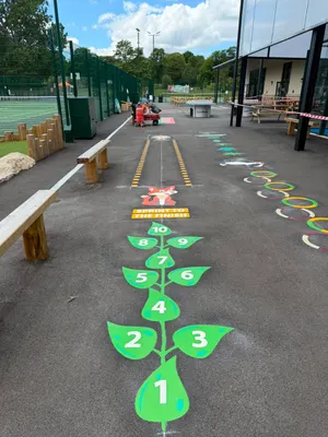 Leafy beanstalk hopscotch marking numbered 1 to 10 leading to a fox sprint track, beside fenced tennis courts and a pavilion