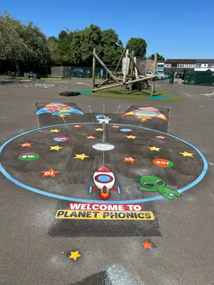 Welcome to Planet Phonics circle marking with phonics sounds on stars, a rocket and a green alien, by a wooden climbing frame