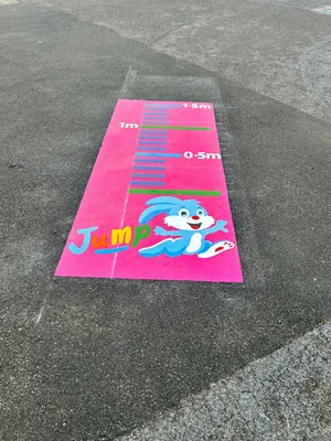 Pink standing long jump marking with a cartoon blue rabbit, the word Jump and distance lines up to 1.5m on grey tarmac