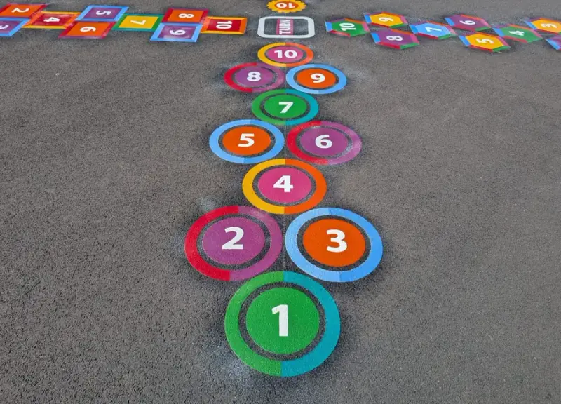 Close-up of a ringed 1 to 10 hopscotch marking ending at a turn box, with diagonal tracks of coloured number squares either side