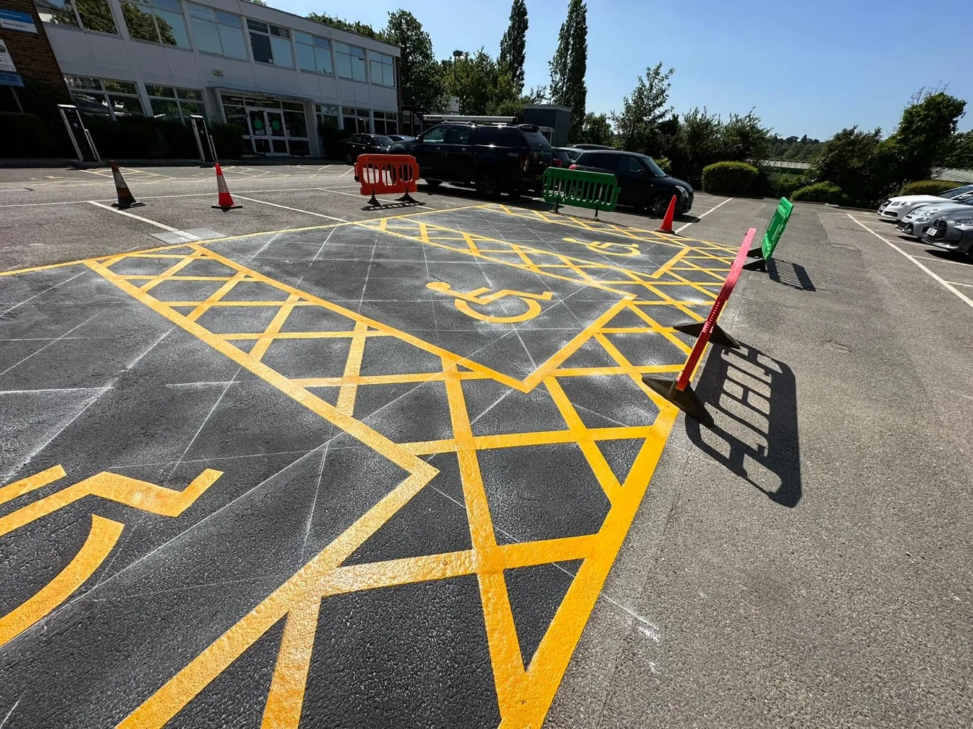 Yellow thermoplastic disabled parking bays with wheelchair symbols and hatched zones freshly marked on a tarmac car park