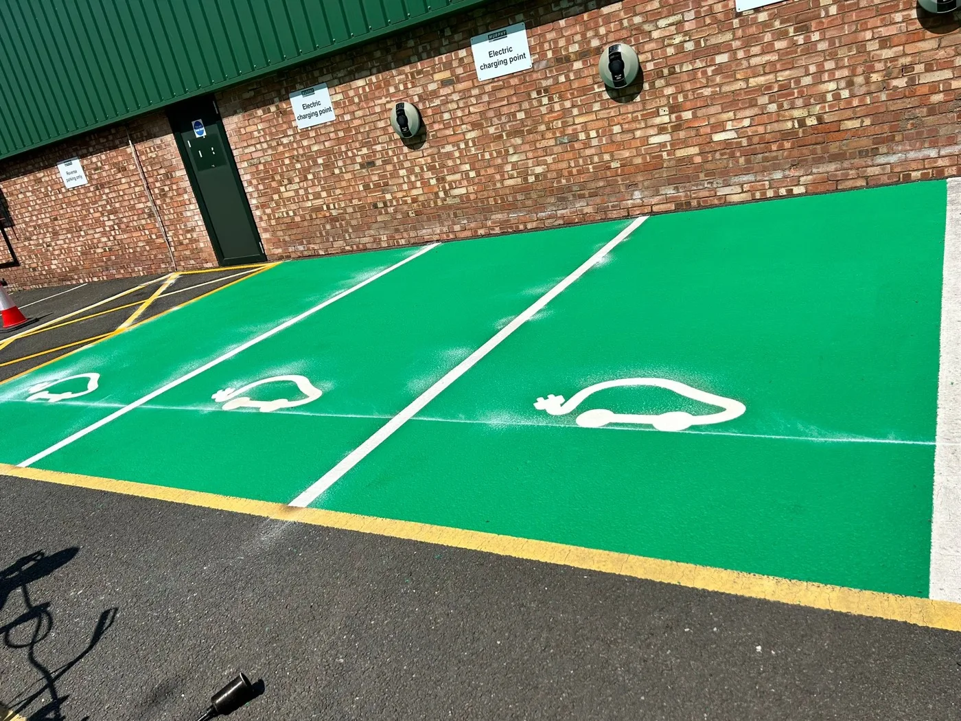 Three green-surfaced electric vehicle charging bays with white car symbols beside wall-mounted charging points