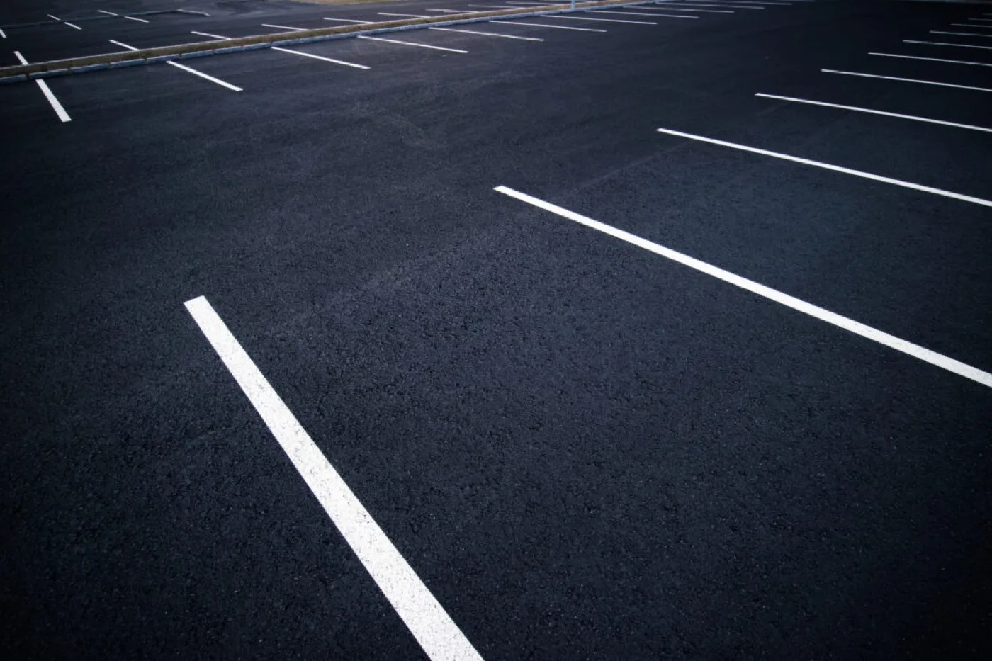 Crisp white parking bay lines newly marked across a dark, freshly surfaced tarmac car park