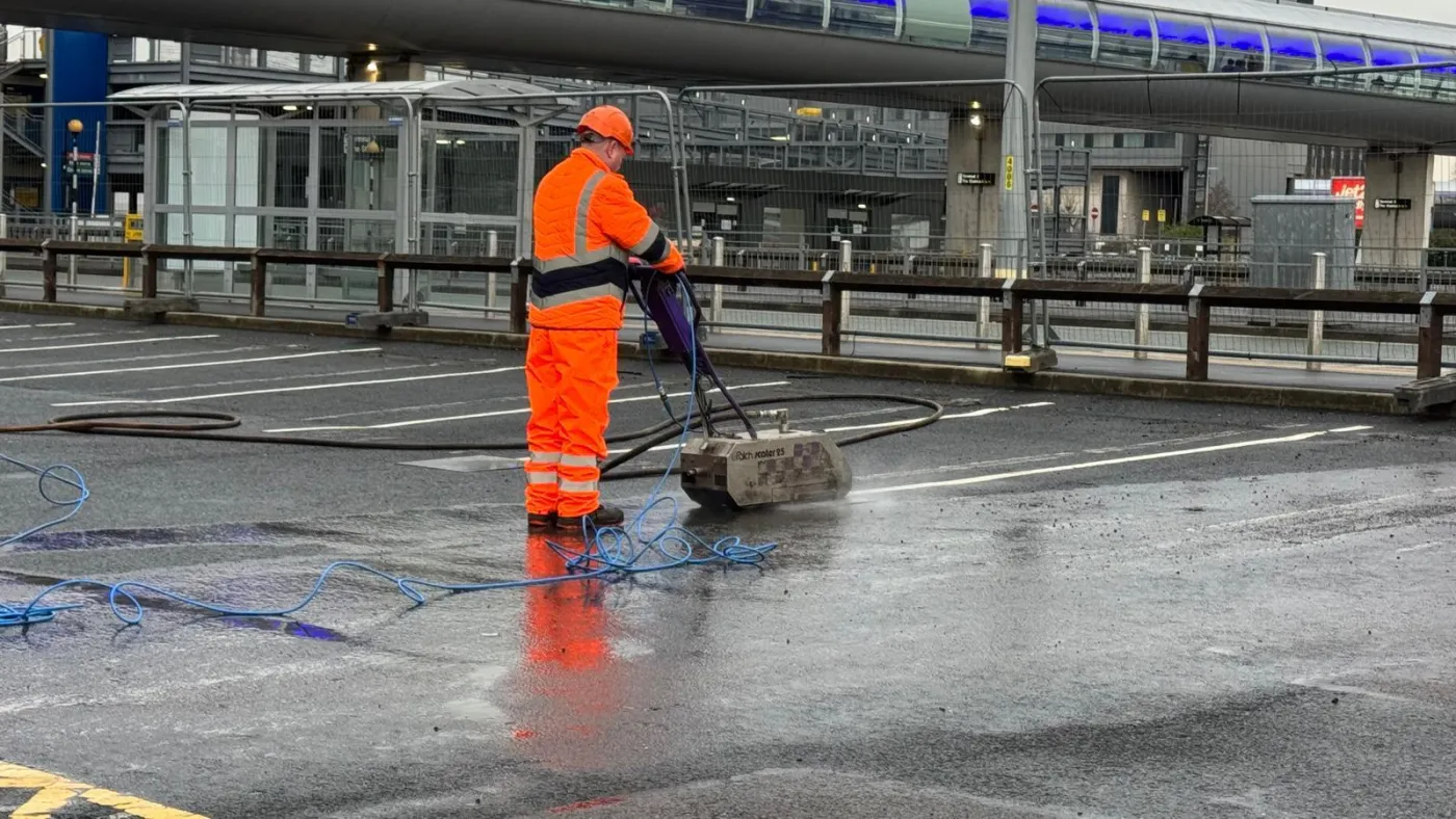 Worker in orange overalls running a Fisch Scaler planing machine to strip white road markings off wet tarmac