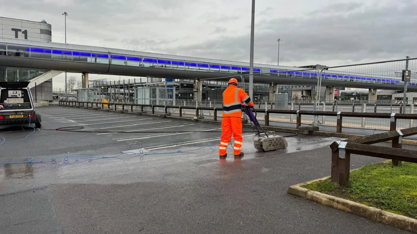 Operative guiding a surface planer along a parking bay, the white line partly scoured away on wet asphalt