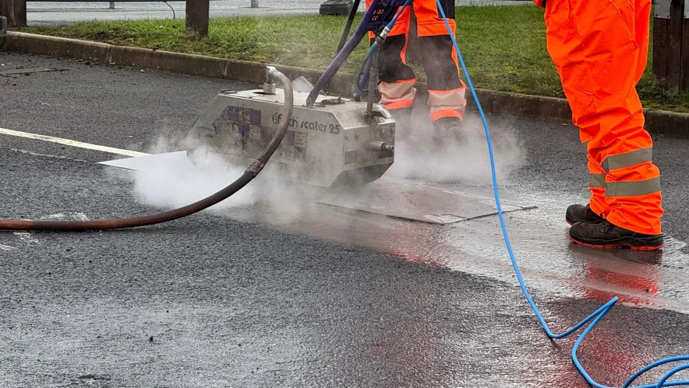 Close-up of the Fisch Scaler 25 machine throwing spray and steam as it grinds a white line off tarmac
