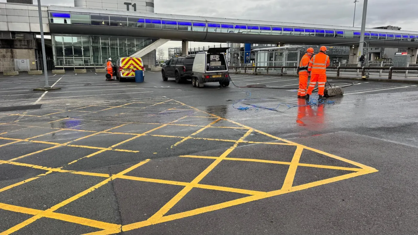 Two operatives finishing removal of yellow cross-hatch markings, ghost outlines still faintly visible on the asphalt