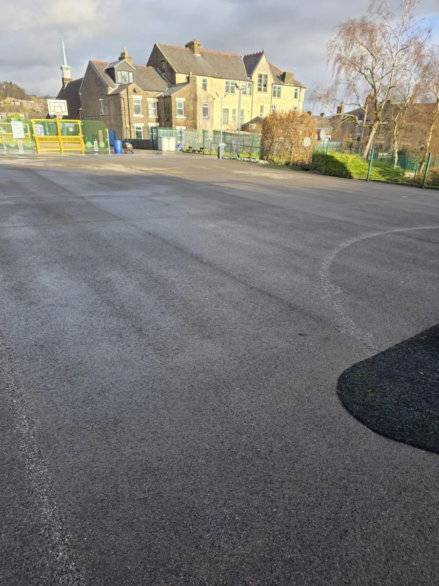 Cleared school playground tarmac after marking removal, only a faint pale arc left on the dark surface
