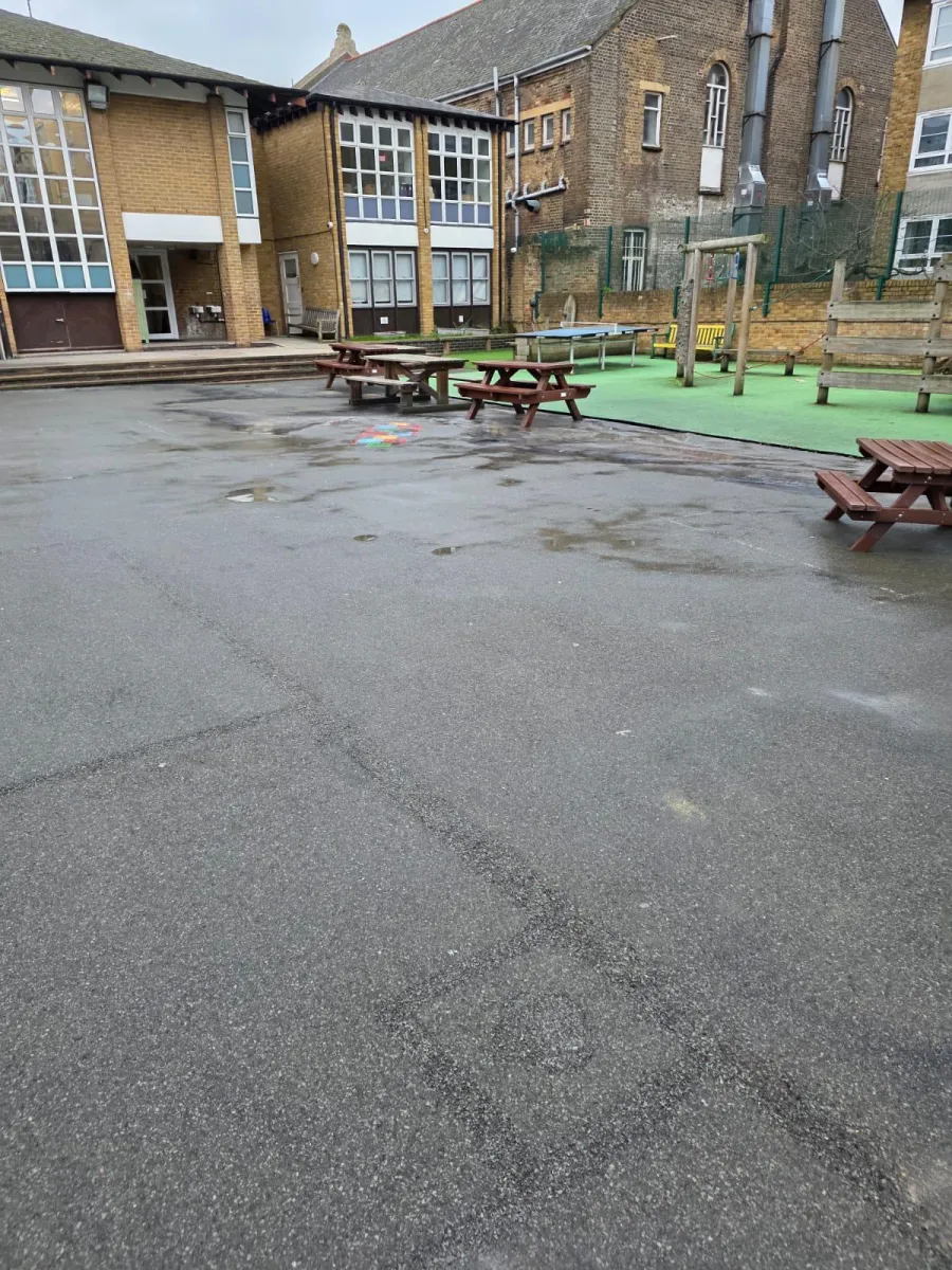 School yard tarmac after removal with one small coloured graphic remaining near the picnic benches