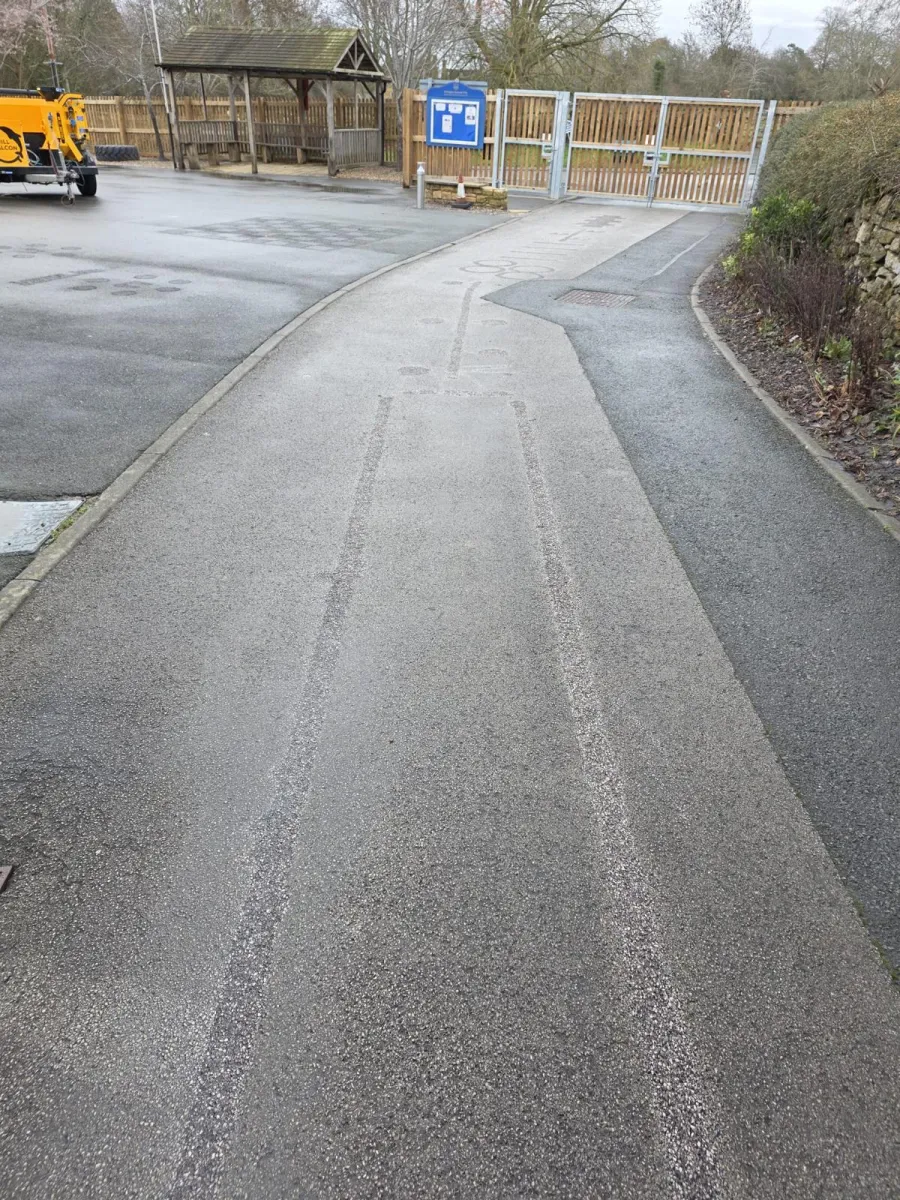 Pale scoured tracks left along a tarmac path where line markings have been planed away near the gate